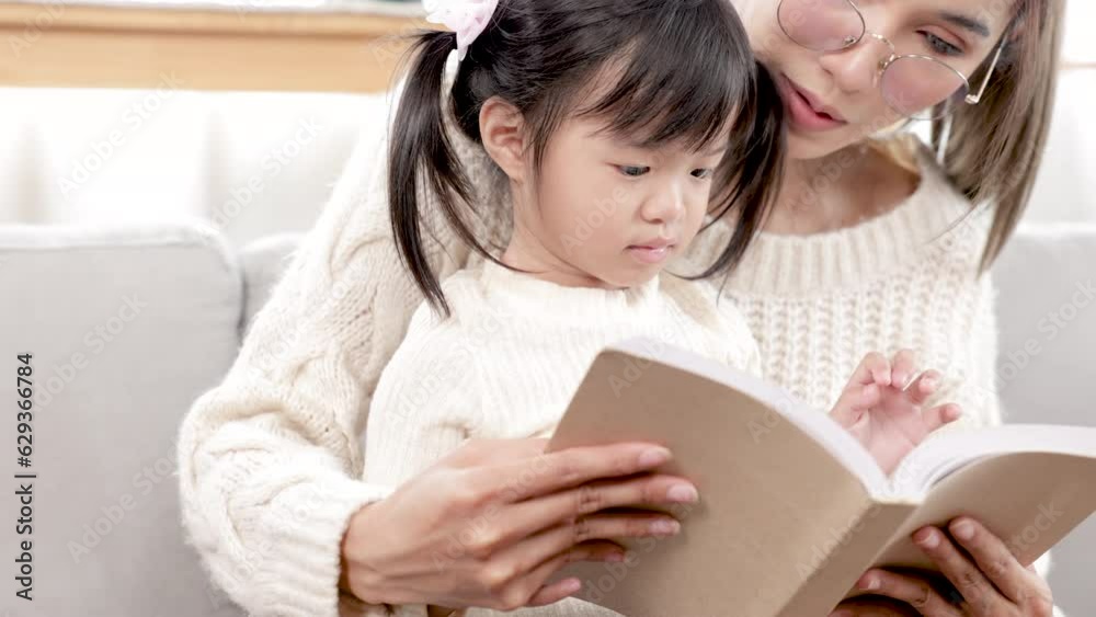 Asian beautiful pregnant mother reads a book with her eldest daughter in the living room during their leisure time, mom teaching baby to read, Telling stories to little child. family happiness concept Asian beautiful pregnant mother reads a book with her eldest daughter in the living room during their leisure time, mom teaching baby to read, Telling stories to little child. family happiness concept