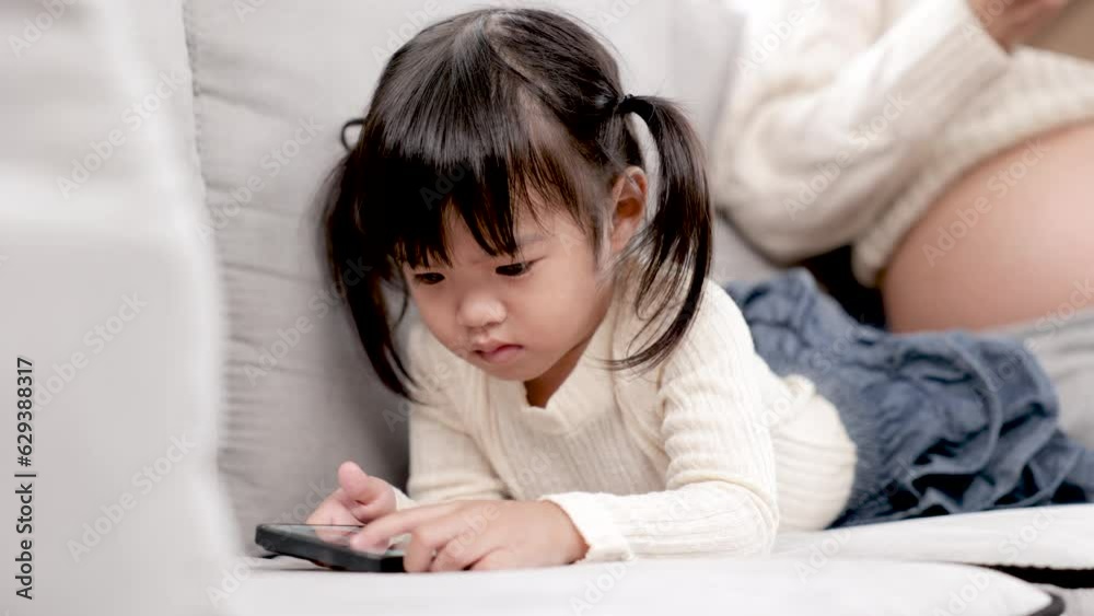 4k, Close up adorable preschool girl watching smartphone lying down near pregnancy mother, mom and daughter bonding relationship concept, motherhood lifestyle take care kids in cozy living room 4k, Close up adorable preschool girl watching smartphone lying down near pregnancy mother, mom and daughter bonding relationship concept, motherhood lifestyle take care kids in cozy living room
