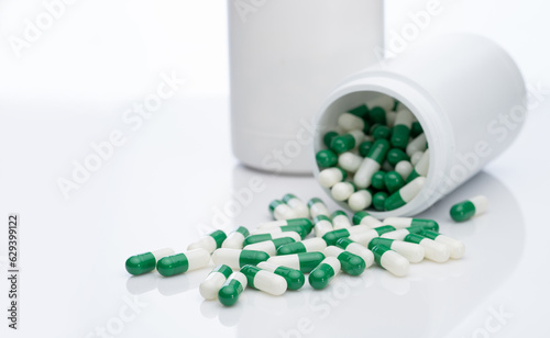 Green and white capsule pills spilled out of a white plastic bottle. Pharmaceutical industry. Prescription drug. Healthcare and medicine. Pharmacy product. Pharmaceutics. Capsule pill manufacture. photo