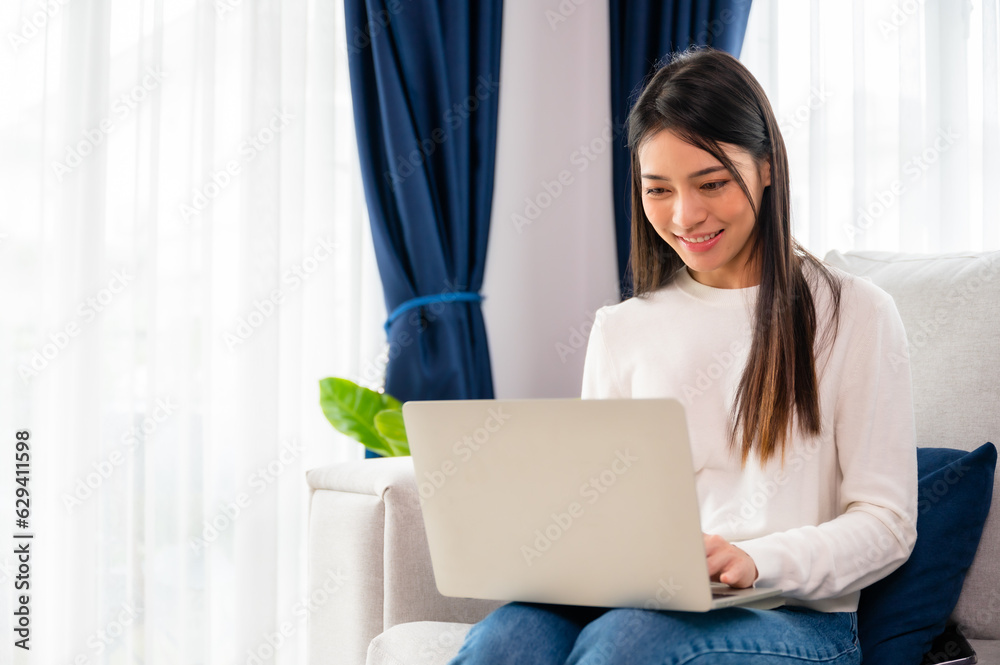 Young asian woman using laptop while seated on couch at home Young asian woman using laptop while seated on couch at home