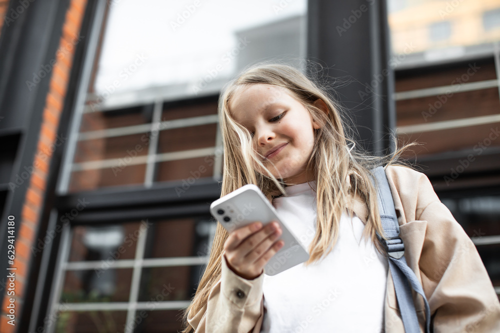 Fototapeta premium Back to school. A schoolgirl is looking for something on the smartphone screen