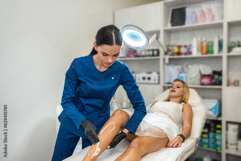 Obraz premium female client legs applying wax contact gel before the procedure of removal unwanted hair in spa