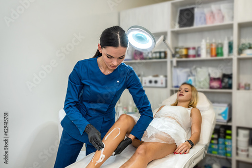 female client legs applying wax contact gel before the procedure of removal unwanted hair in spa