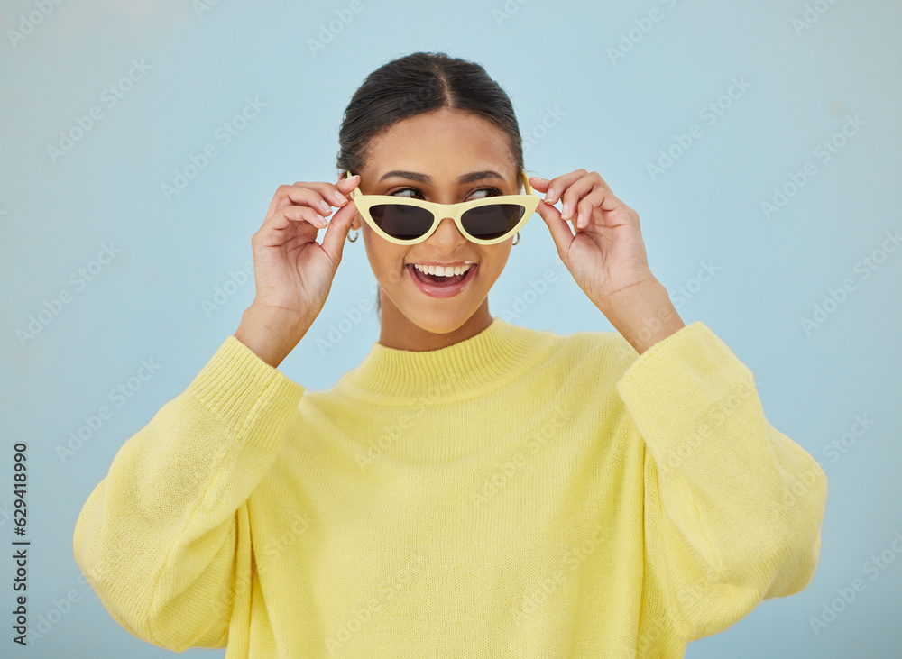 Happy, sunglasses and young woman in a studio with a casual, stylish and cool sweater outfit. Happiness, smile and female model with trendy style and fashion accessory isolated by a blue background. Happy, sunglasses and young woman in a studio with a casual, stylish and cool sweater outfit. Happiness, smile and female model with trendy style and fashion accessory isolated by a blue background.