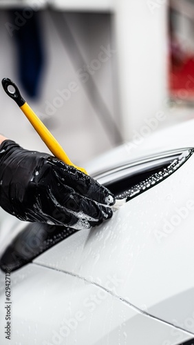 Obraz na płótnie Employee of a car detailing studio or car wash carefully cleans the area around the front headlight with a brush in a white car w salonie