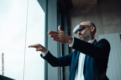 Mature businessman gesturing with virtual reality simulators in office