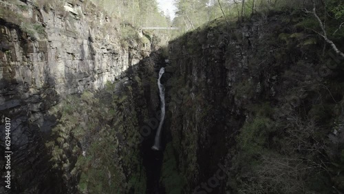 Drone shot flying away from big waterfall inside narrow and rocky Corrieshalloch gorge in Scottish Highlands photo