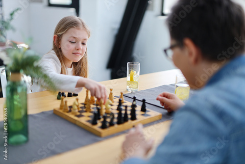 Family of mother and daughter plays chess together in their living room.