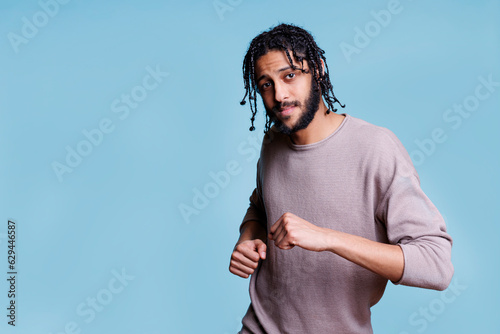 Carefree arab man dancing, making moves with hands and looking at camera. Young handsome arabian person wearing casual clothes in good mood enjoying party and relaxing portrait