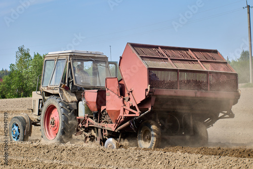 Spring sowing on farmer field, an agricultural wheeled tractor with hitched potato planter rides on arable land.