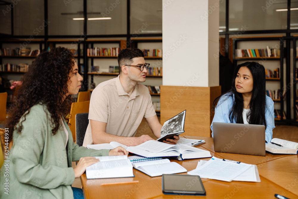 Group of students preparing for exams together while sitting at table in library Group of students preparing for exams together while sitting at table in library