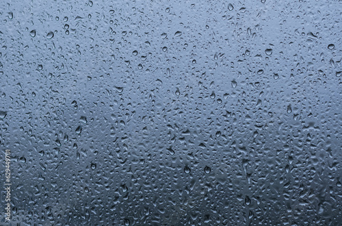 Rain drop on glass window with blue background in monsoon season.