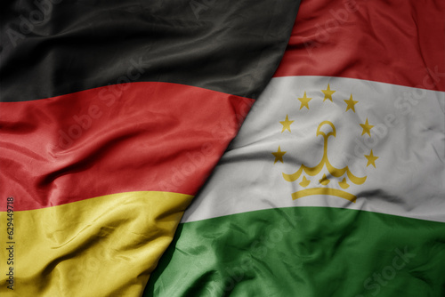 big waving realistic national colorful flag of germany and national flag of tajikistan .