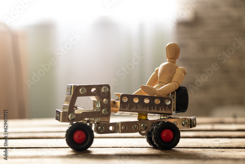 A small wooden man sits on a track made of metal pats on a wooden board, children's toys
