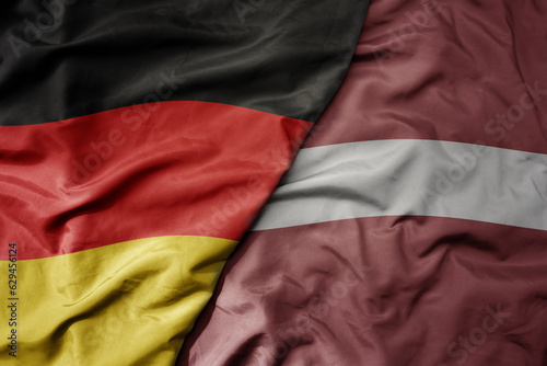big waving realistic national colorful flag of germany and national flag of latvia .