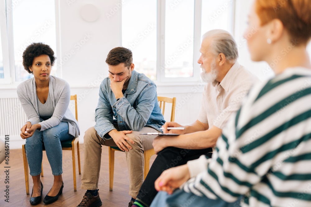 Side view of serious senior adult male group leader speaking on teambuilding meeting. Business team sitting on chairs in circle, talking, discussing project idea, brainstorming, listening to male boss Side view of serious senior adult male group leader speaking on teambuilding meeting. Business team sitting on chairs in circle, talking, discussing project idea, brainstorming, listening to male boss