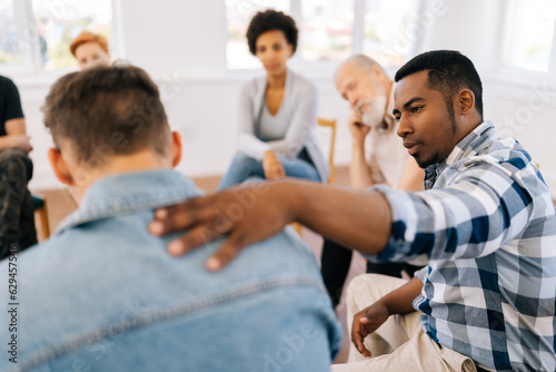 Closeup back view of unrecognizable sad man sharing life problem grief with multiracial people in modern mental health support group session in rehab center. Concept of mental health, psychotherapy.