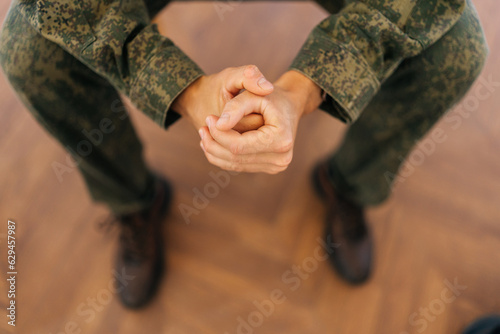 Close-up high-angle view of unrecognizable soldier male in camouflage uniform tightly clenching fists sitting in circle during PTSD group therapy session. Concept of mental health, psychotherapy