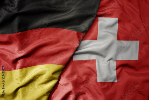 big waving realistic national colorful flag of germany and national flag of switzerland .