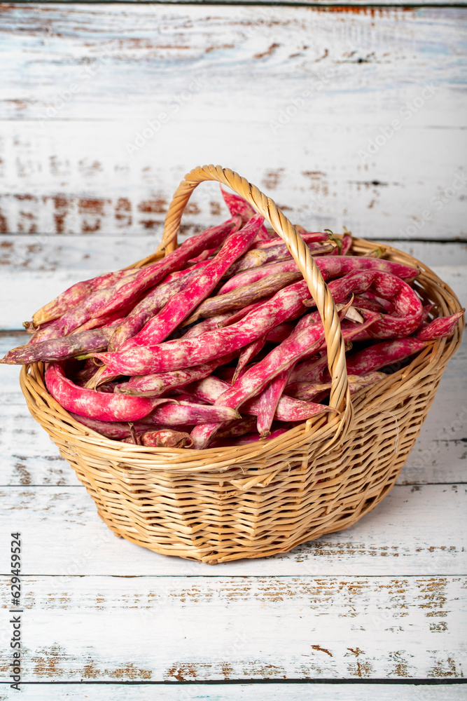 Fresh kidney beans in a wicker basket over wooden background. Pinto beans or cranberry beans harvest season concept. Vegetables for a healthy diet. Close up