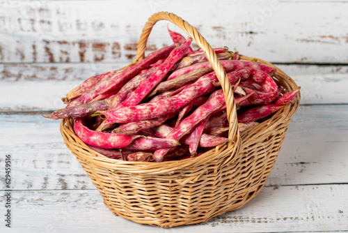 Fresh kidney beans in a wicker basket over wooden background. Pinto beans or cranberry beans harvest season concept. Vegetables for a healthy diet