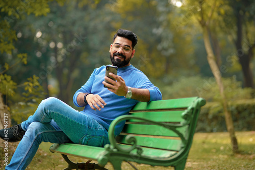young indian man using smartphone at park. © Niks Ads