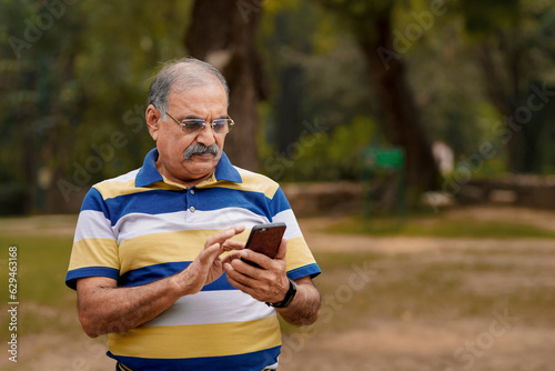 Old indian man using smartphone at park.