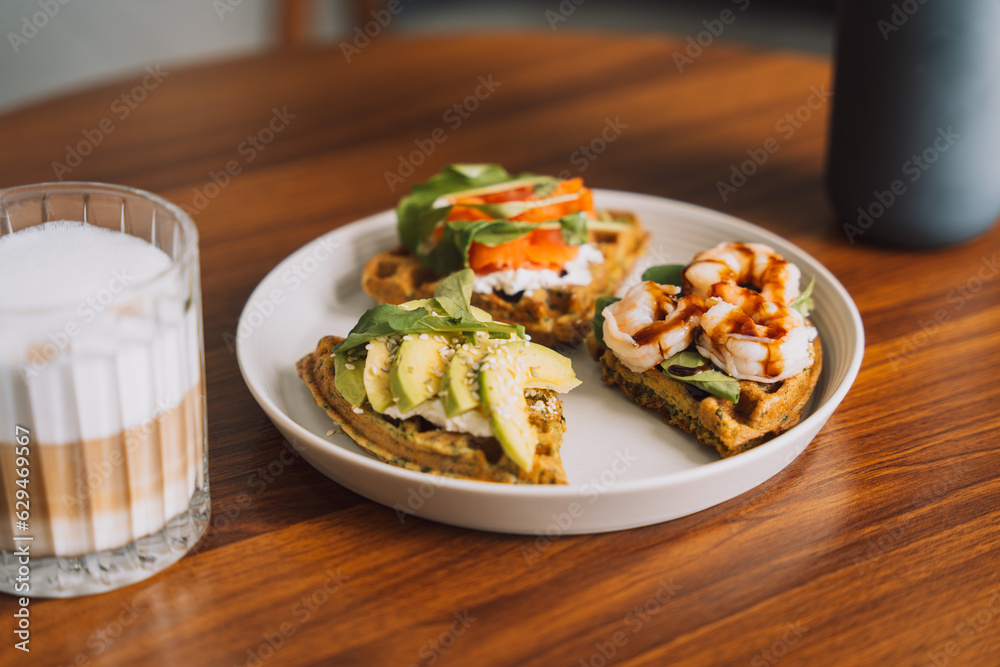 Waffles with seafood and avocado on a white plate with coffee.