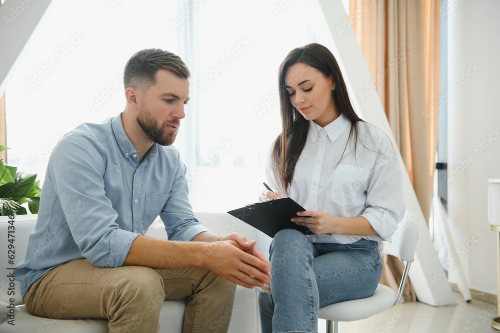 Psychologist talking with patient on therapy session. Depressed man speaking to a therapist while she is taking notes Psychologist talking with patient on therapy session. Depressed man speaking to a therapist while she is taking notes