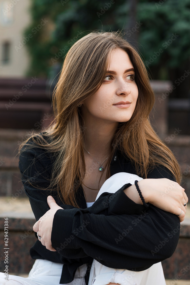 Portrait of a young and attractive happy girl sitting on the steps on a summer day in casual clothes.
