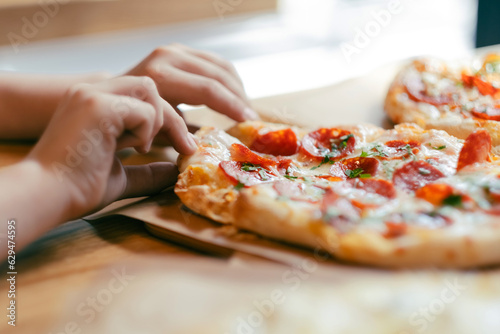 Child hand taking a slice of fresh delicious pepperoni pizza served on craft paper. Selective focus.