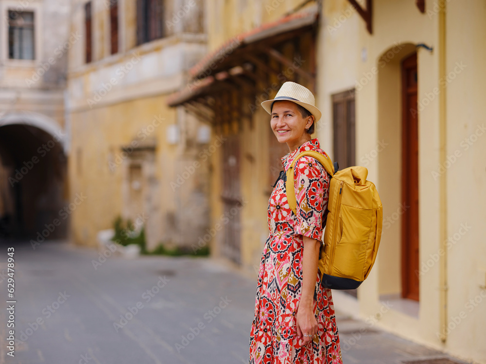 Young Asian woman in red dress and backpack walks and looks at cozy narrow streets of old city. Tourism, vacation, and discovery concept, female traveler visiting southern Europe, Rhodes island Greece Young Asian woman in red dress and backpack walks and looks at cozy narrow streets of old city. Tourism, vacation, and discovery concept, female traveler visiting southern Europe, Rhodes island Greece