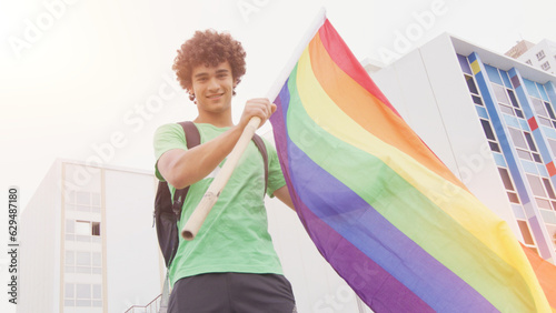 Smiling handsome young man with LGBT flag in his hands