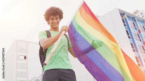 Smiling handsome young man with LGBT flag in his hands