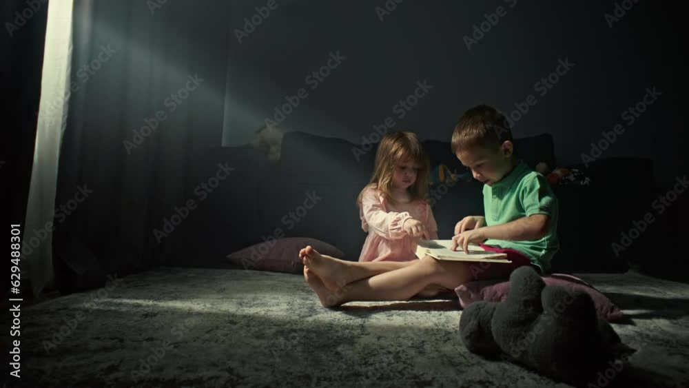 The boy holds a book in his hands and reads it. The children play house on the floor together and the brother learns to read with the sister. High quality 4k footage The boy holds a book in his hands and reads it. The children play house on the floor together and the brother learns to read with the sister. High quality 4k footage
