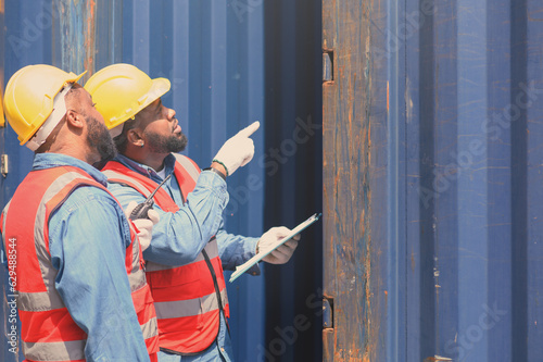 Two Engineers or foreman container cargo wearing white hardhat and safety vests checking stock into container for loading from Cargo freight ship for import export. industry of logistic concept.