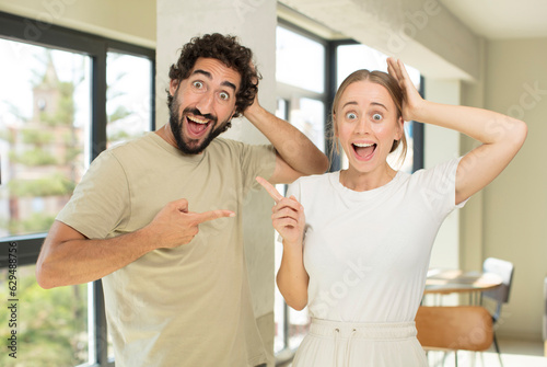 young adult couple laughing, looking happy, positive and surprised, realizing a great idea pointing to lateral copy space