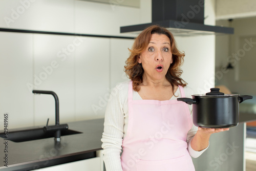 middle age pretty woman feeling extremely shocked and surprised. cooking at home concept