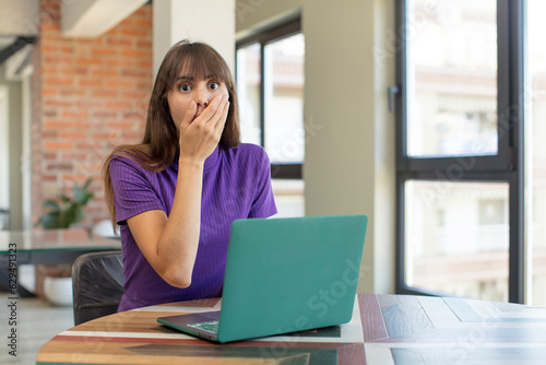 young pretty woman covering mouth with a hand and shocked or surprised expression. desk laptop concept
