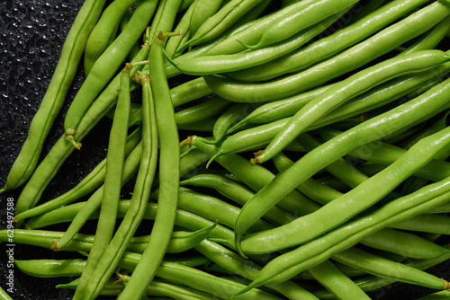 Heap of green pods of raw asparagus beans on a dark background. Top view.