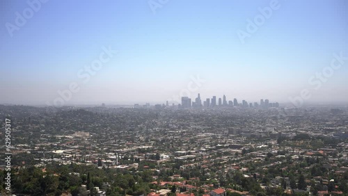Zoomed in panning right view of the LA skyline from the Griffith Observatory with blue sky and lots of houses and neighborhoods.
