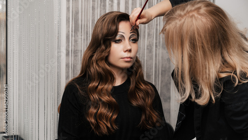 A makeup artist makes eye makeup art for a young girl in a beauty salon. The concept of celebrating Halloween. Unusual makeup.