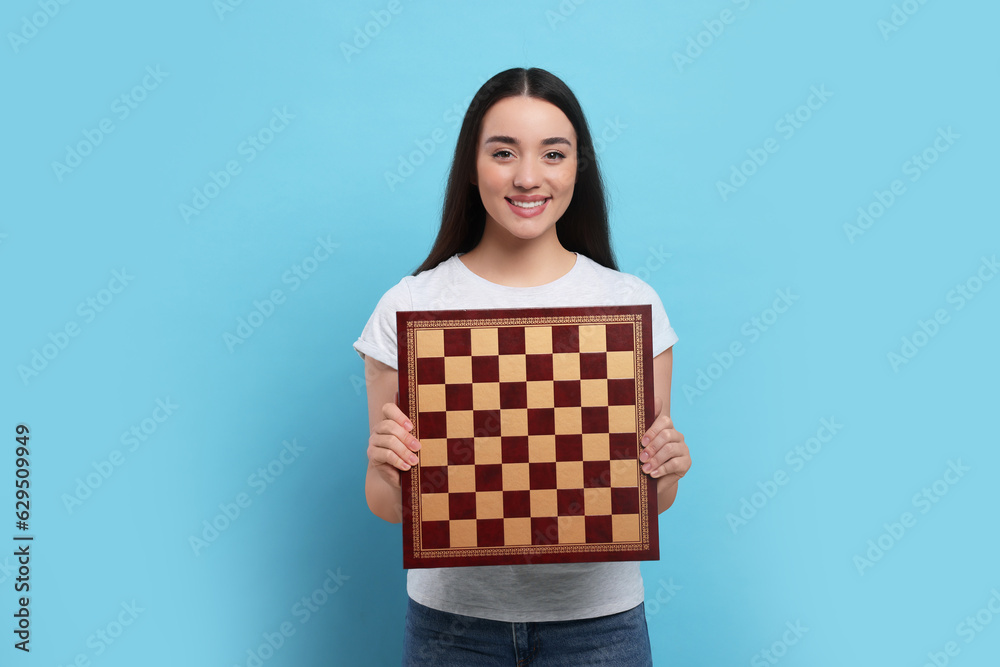 Happy woman with chessboard on light blue background Happy woman with chessboard on light blue background