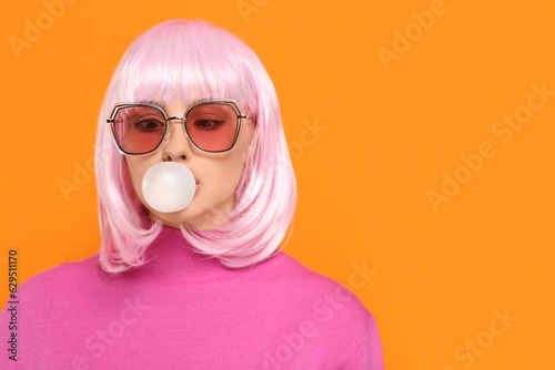 Beautiful woman in sunglasses blowing bubble gum on orange background, space for text photo