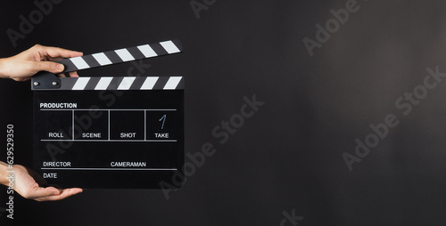 Hand is holding Black clap board or movie slate use in video production , movie ,film, cinema industry on black background.It have write in number.