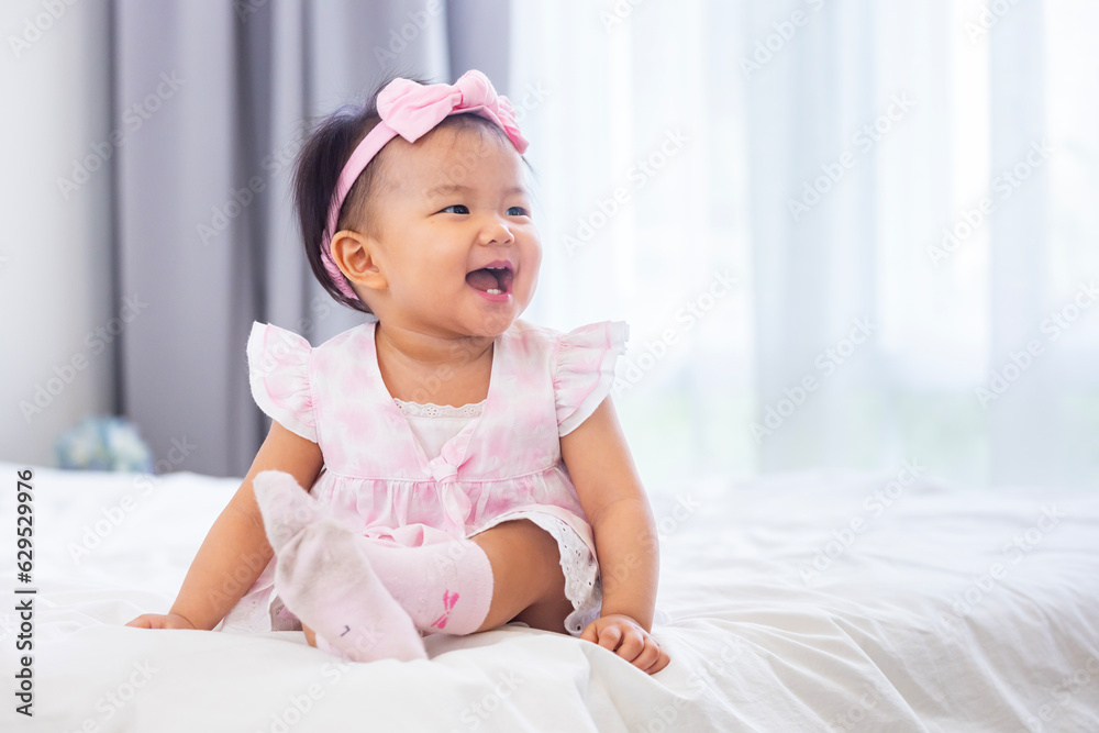 Asian baby toddler in cute pink dress is smiling while sitting on the bed with happiness for healthy kid and adorable girl portrait usage Asian baby toddler in cute pink dress is smiling while sitting on the bed with happiness for healthy kid and adorable girl portrait usage