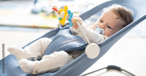 Принти на полотні Adorable 5 months old baby boy sitting in his swing rocking chair, playing with rotating toys