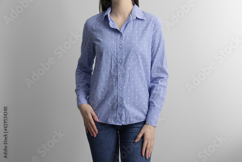 Woman wearing wrinkled light blue polka dot blouse on light grey background, closeup