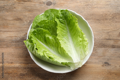 Bilde på lerret Bowl with fresh leaves of green romaine lettuce on wooden table, top view