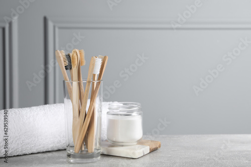 Bamboo toothbrushes, towel and jar of baking soda on light grey table, space for text